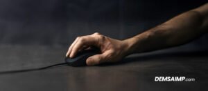 Mano masculina sujetando un mouse negro con cable sobre una superficie oscura, en una fotografía de estilo profesional y enfoque detallado.